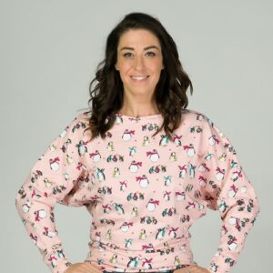 Dark haired lady sitting on a stool with hand on hips wearing a pink top with penguins